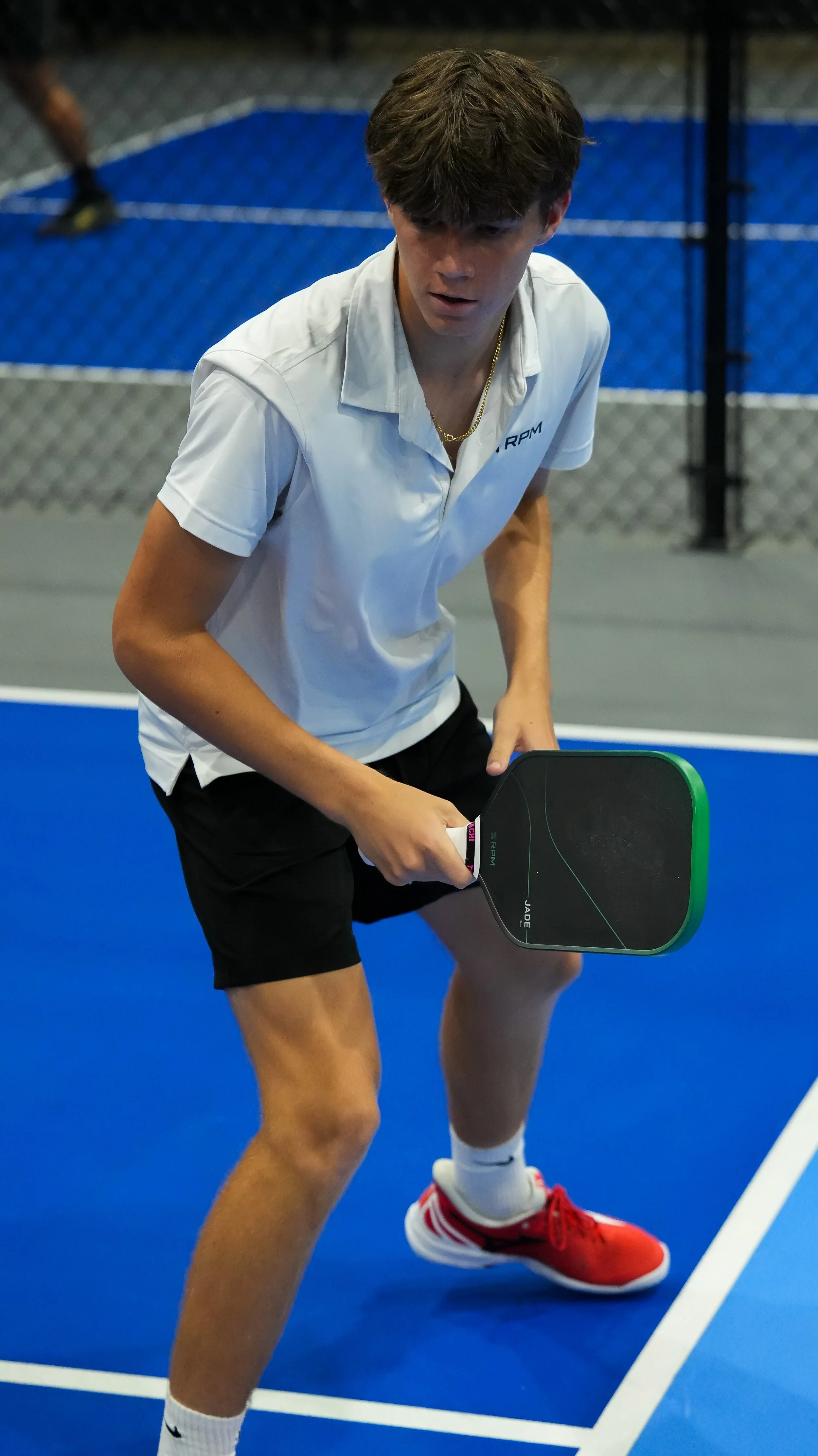 A young man playing pickleball on an indoor court, holding a paddle ready to return the ball.