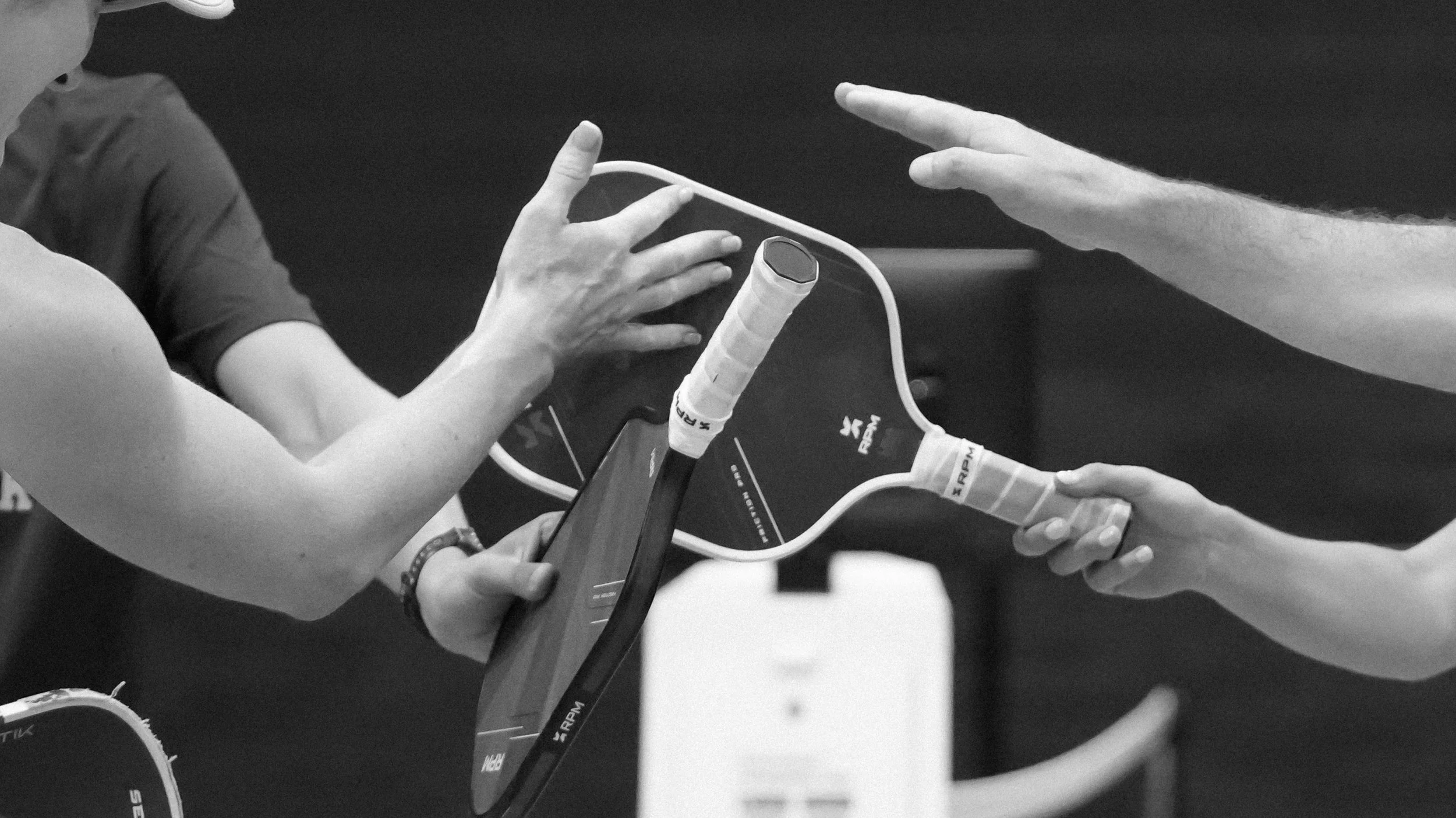 A person holding a paddle tennis racket and another person reaching out to touch it, with a tablet device nearby showing a score or session information.