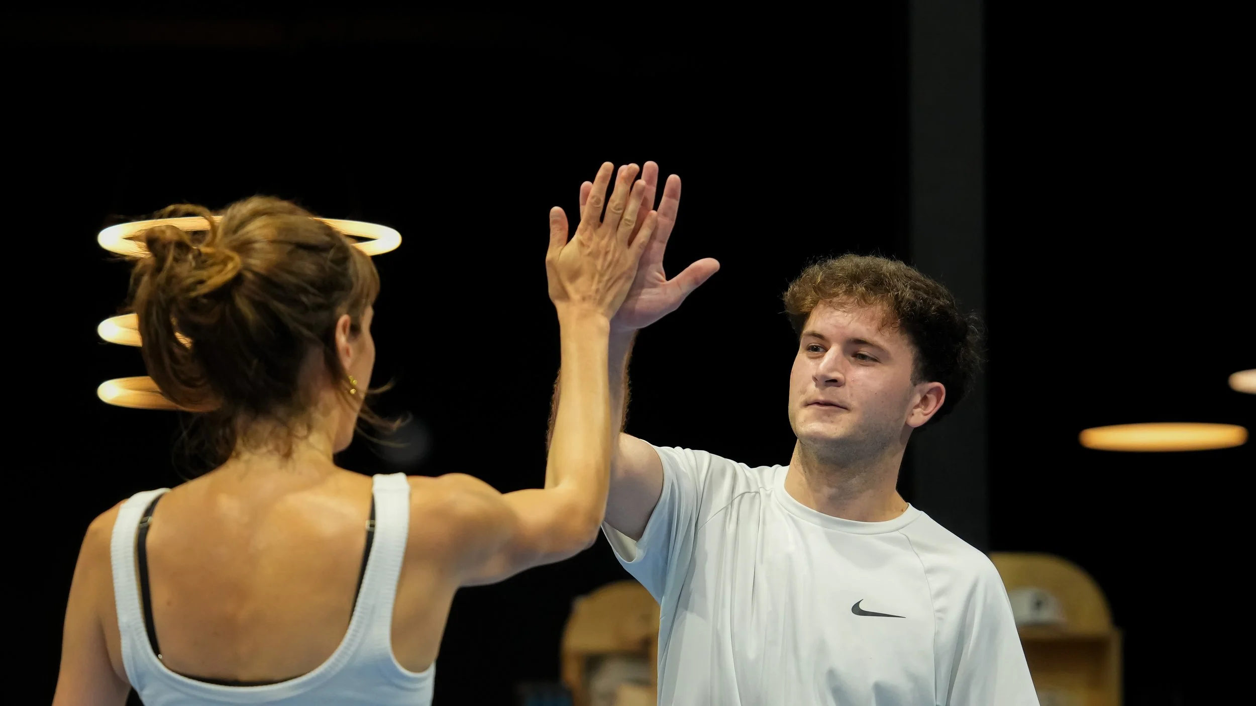A man and woman giving each other a high-five in a dark room with orange oval lights in the background.