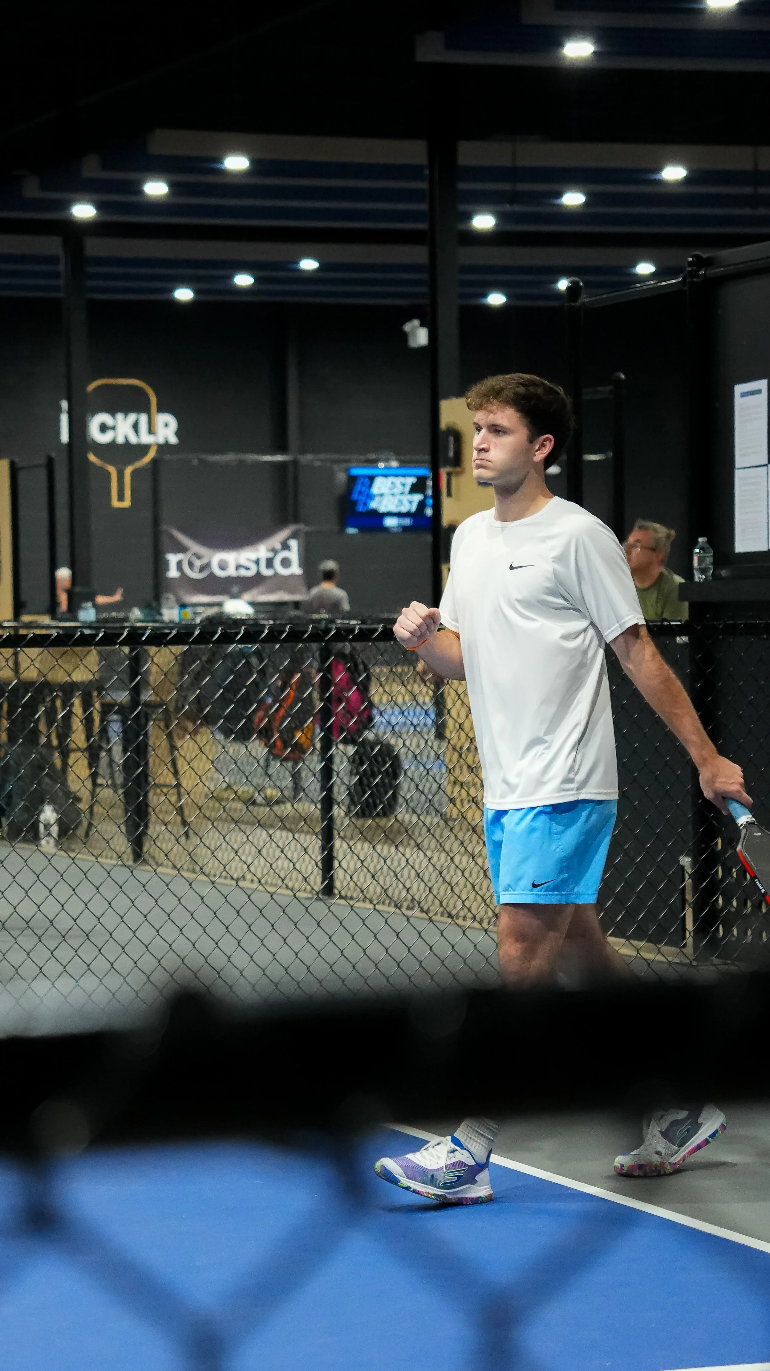 A young man in athletic wear standing next to a tennis court, holding a tennis racquet.