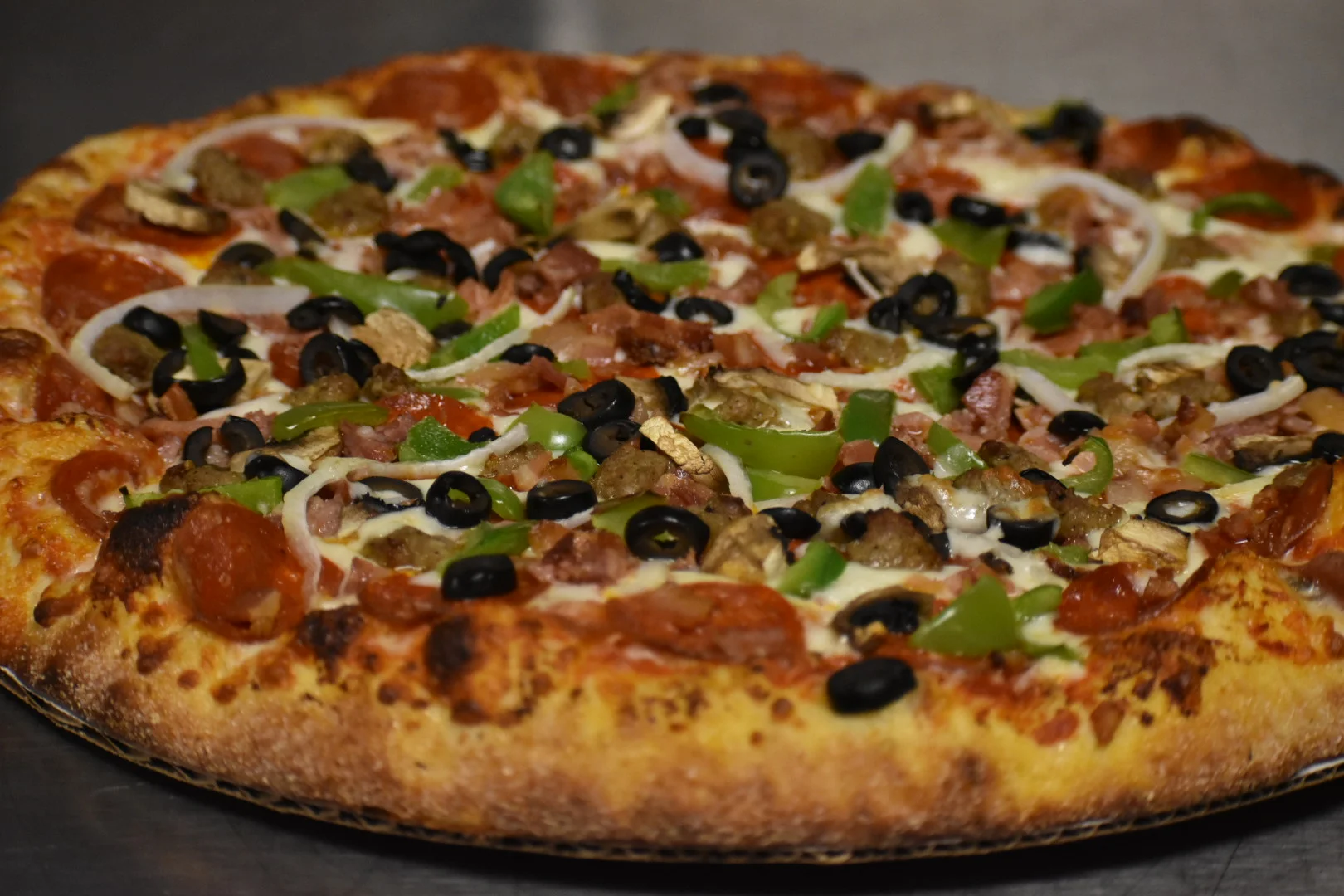 Ford Lanes Bowling Center Bar & Grill - A close-up of pizza with pepperoni, green bell peppers, black olives, ham, and cheese.