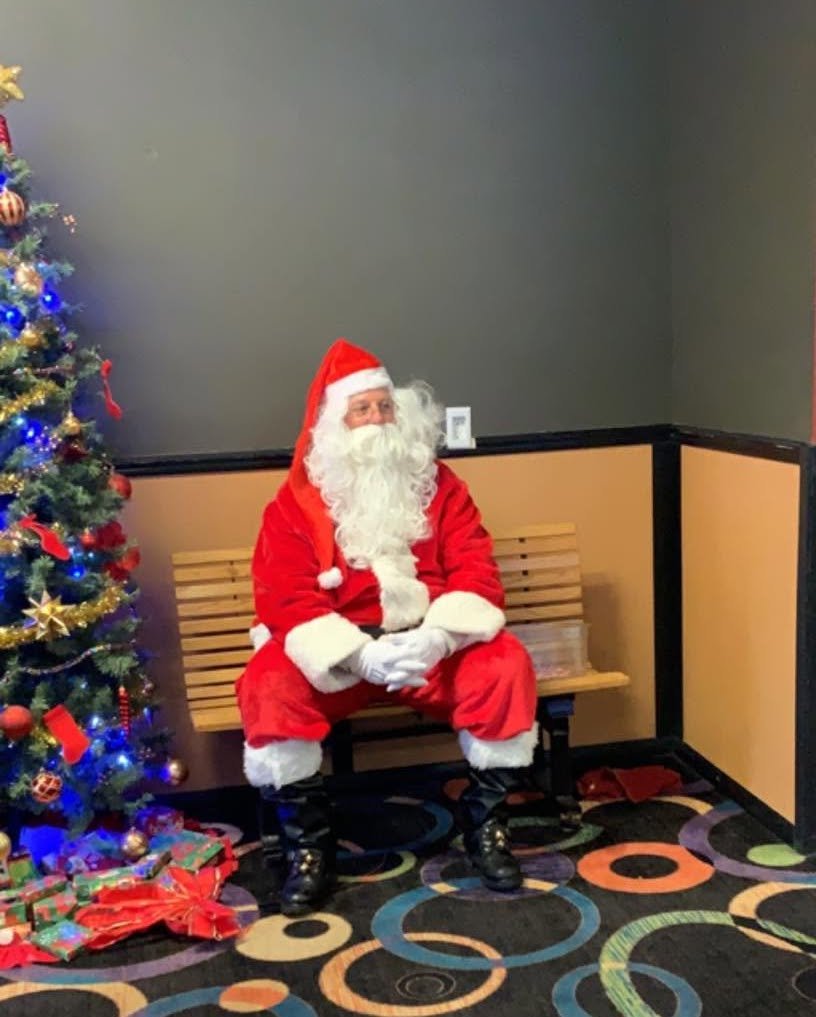 Holiday event venue - Santa Claus sits on a bench next to a decorated Christmas tree with lights and ornaments.