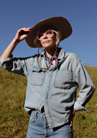 Woman wearing a large straw hat, pink glasses, and denim jacket outdoors on a sunny day.