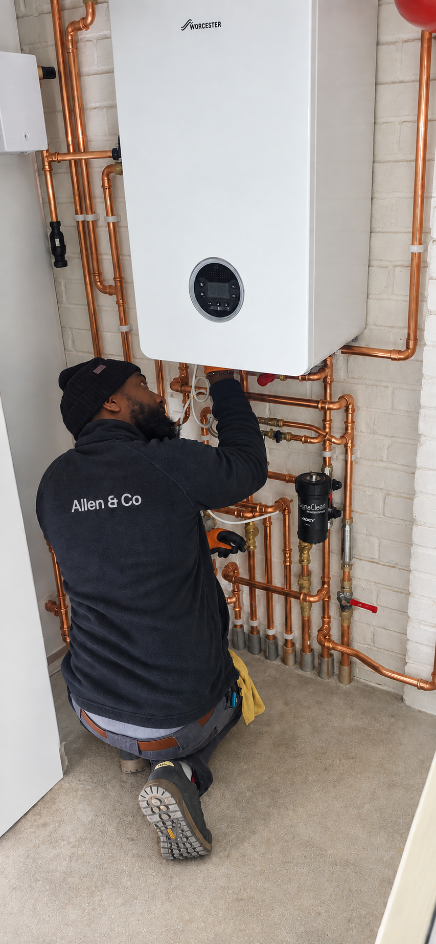 Technician working on a Worcester boiler system with copper piping in a building utility room.