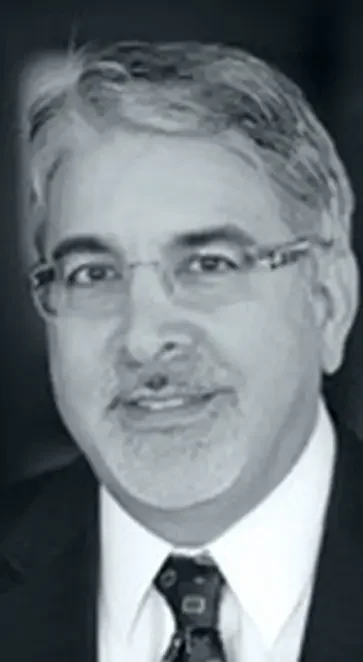 Black and white photo of a man in a suit with glasses, smiling slightly.