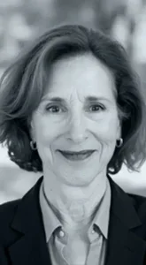 Black and white photo of a woman with short, wavy hair, smiling, wearing a collared shirt and blazer