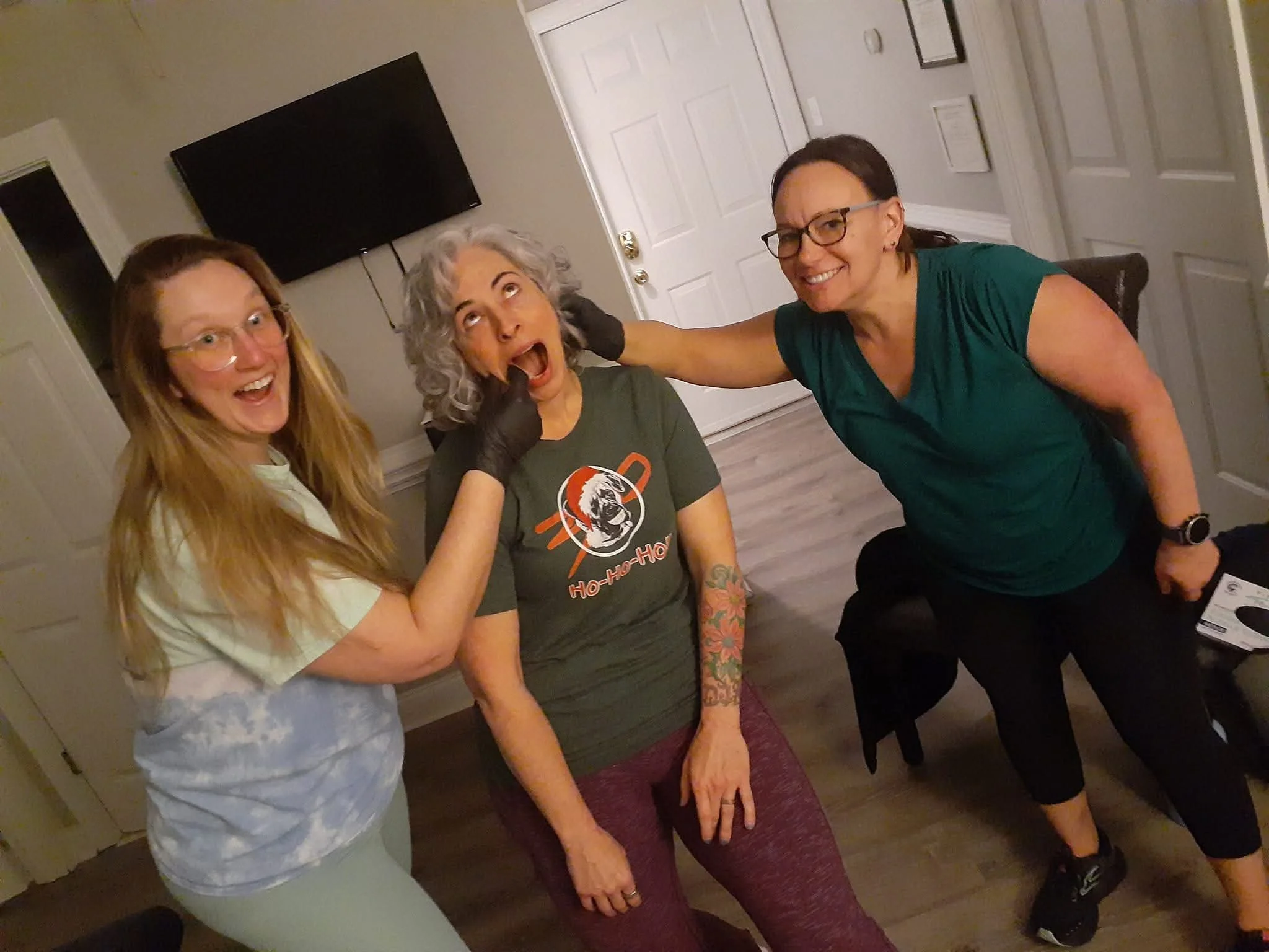 Three women smiling and posing together in a living room.