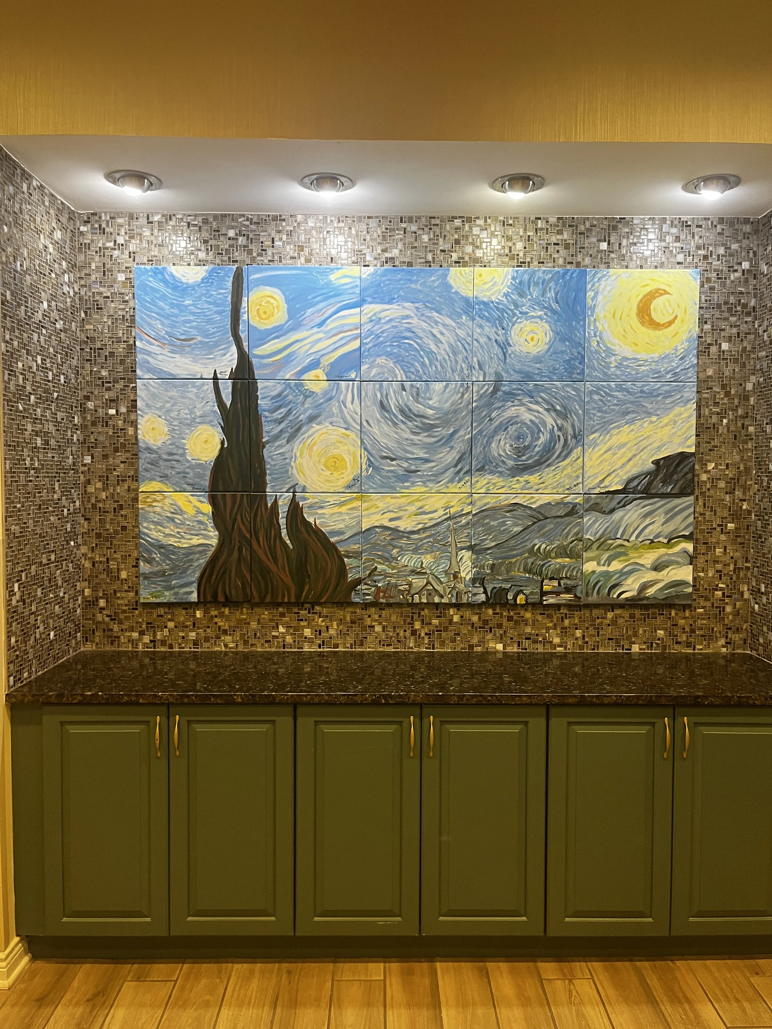 Multi-panel painting of Van Gogh's Starry Night, displayed on a wall above a green kitchen cabinet with gold handles, with mosaic tile backsplash and wooden flooring.