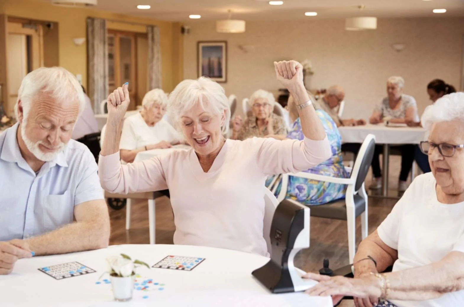 Senior residents playing bingo and cheering at a table during a group activity at an assisted living facility.