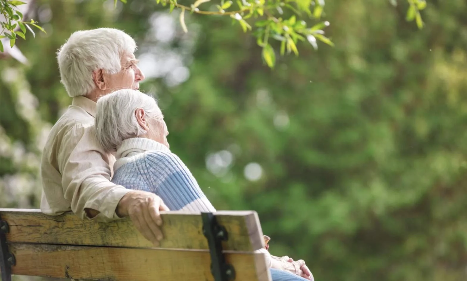 Senior couple sitting on a park bench receiving supportive memory care in a peaceful outdoor environment