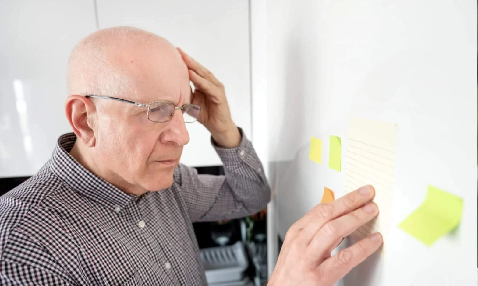 Senior man experiencing memory loss reading sticky note reminders.