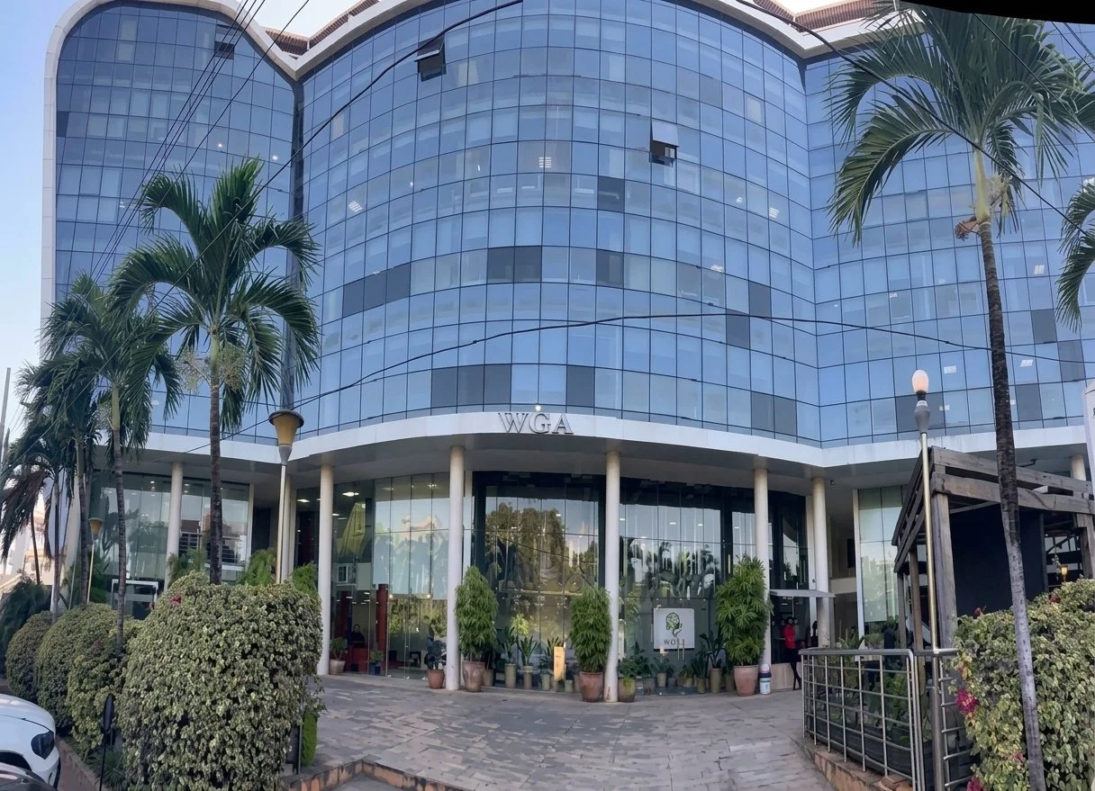 Front view of a modern glass office building with the letters 'WGA' above the entrance, surrounded by palm trees and potted plants.
