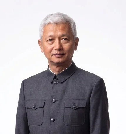 A man with silver hair wearing a dark gray Mao suit, standing against a plain white background.