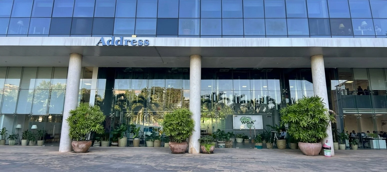 The exterior of a modern office building with a glass facade, large potted plants at the entrance, and a sign that reads "Address" and "WGA."