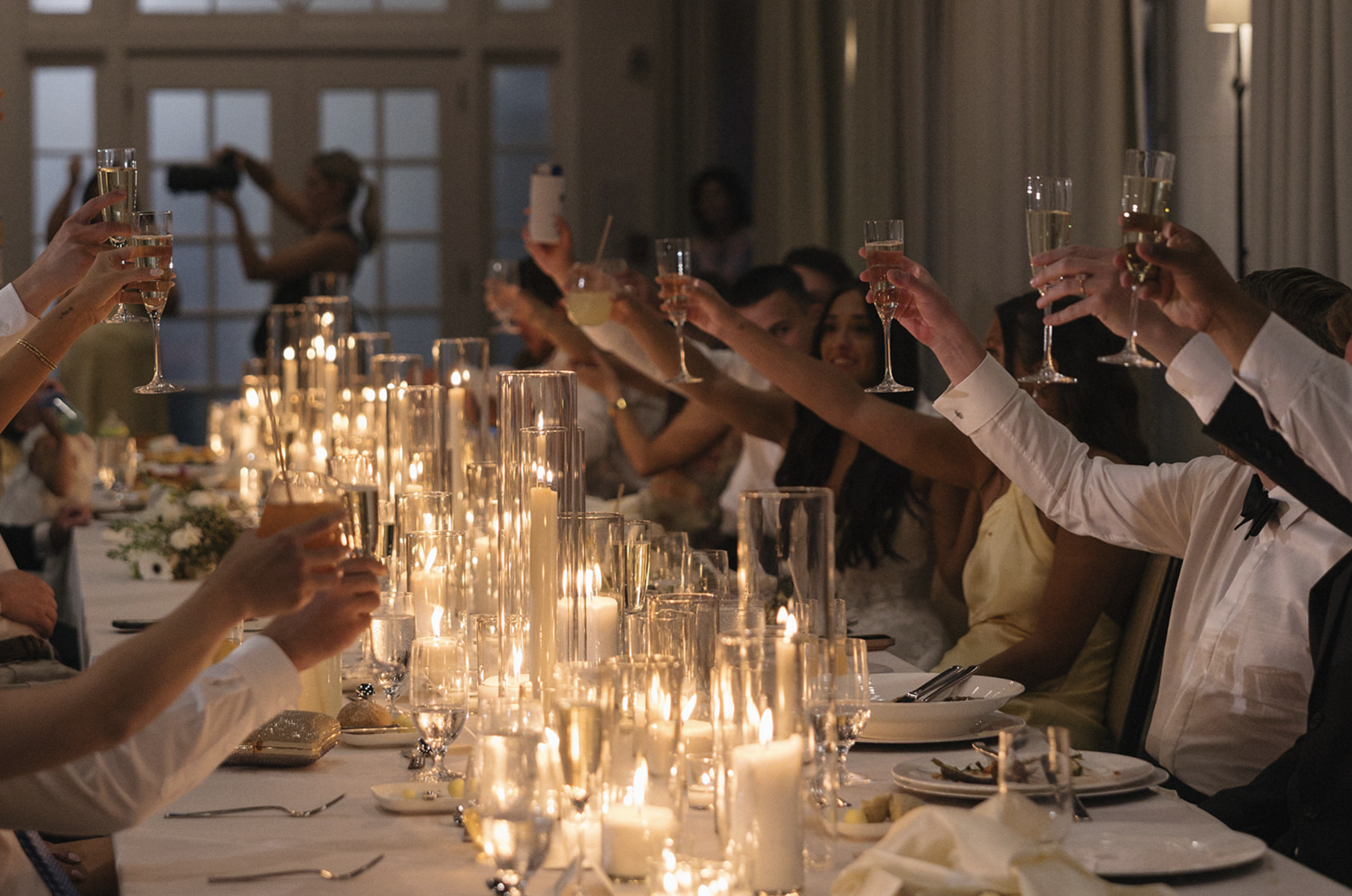 People raising champagne glasses in a toast at a dinner event with lit candles on the table.