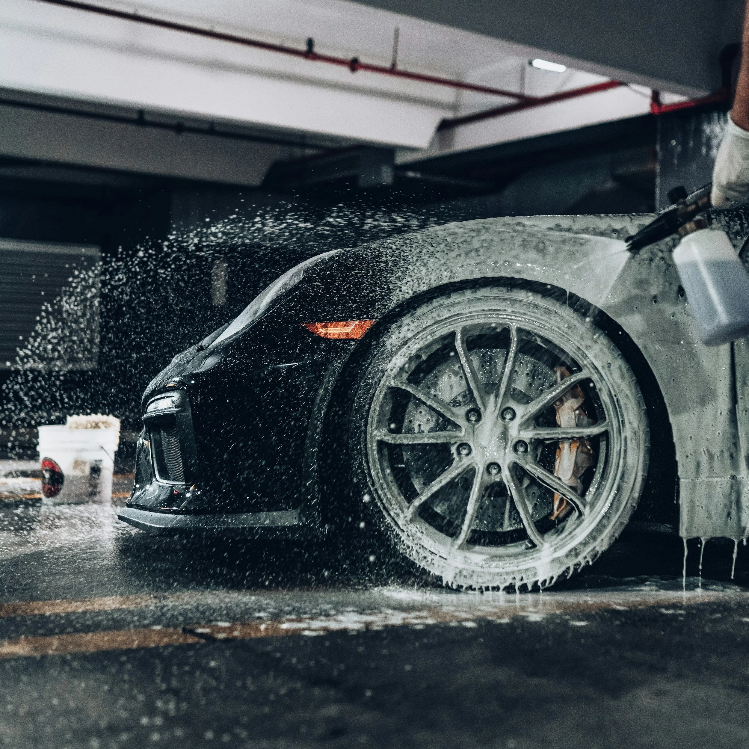 Close-up of a black car with water splashing around its wheels, parked in a garage.