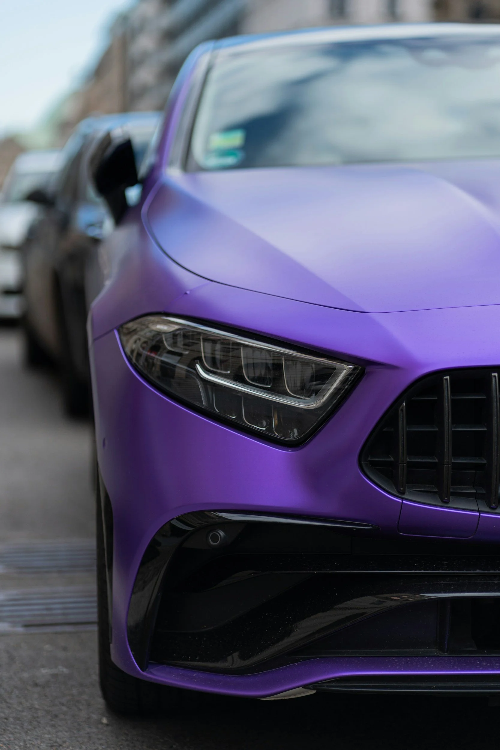 Close-up of a purple luxury car parked outdoors, showing the front headlight, grille, and part of the hood.