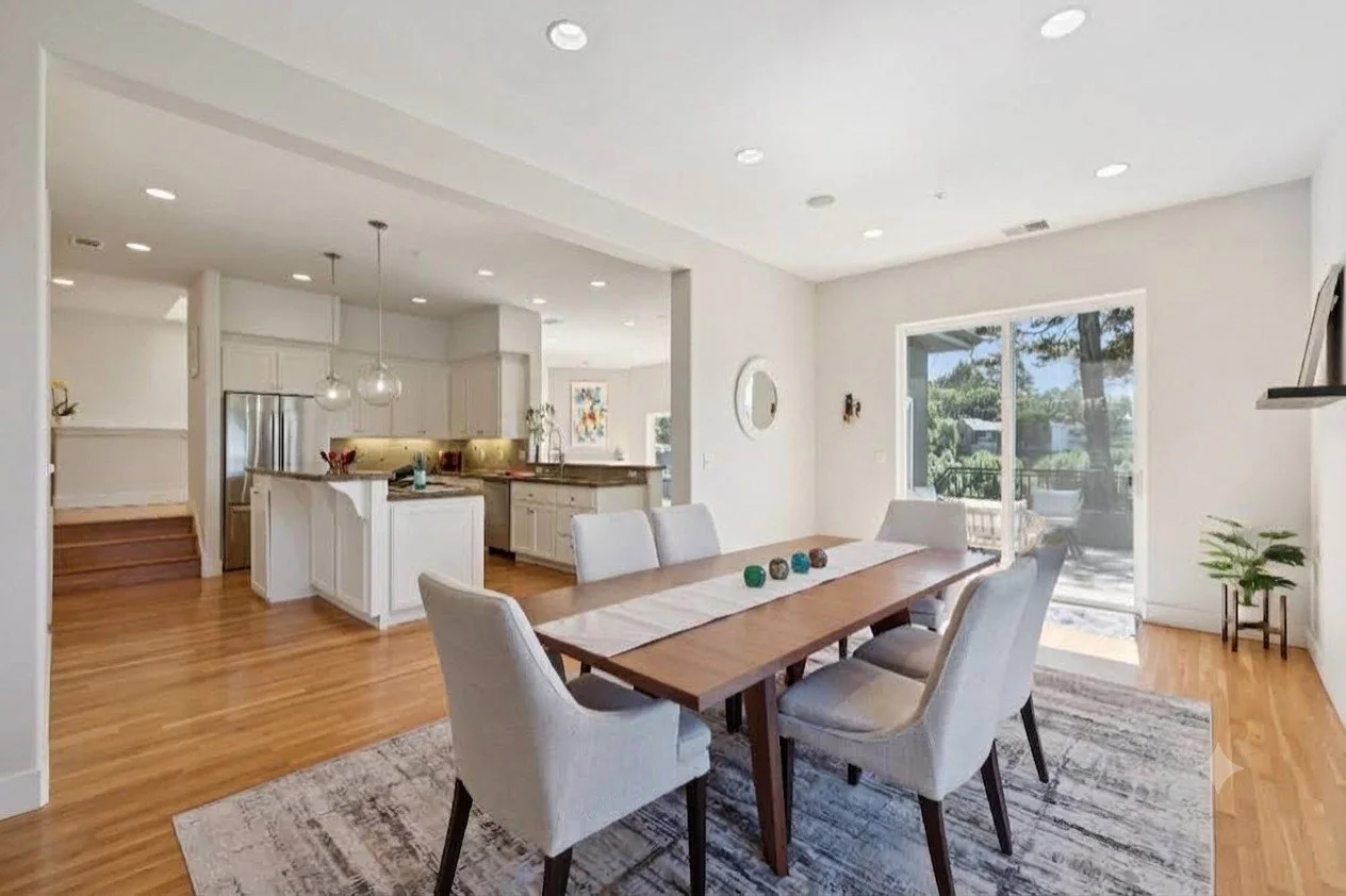 Open-concept white kitchen and dining area with wooden floors, a wooden dining table with chairs, and sliding glass door leading to patio.
