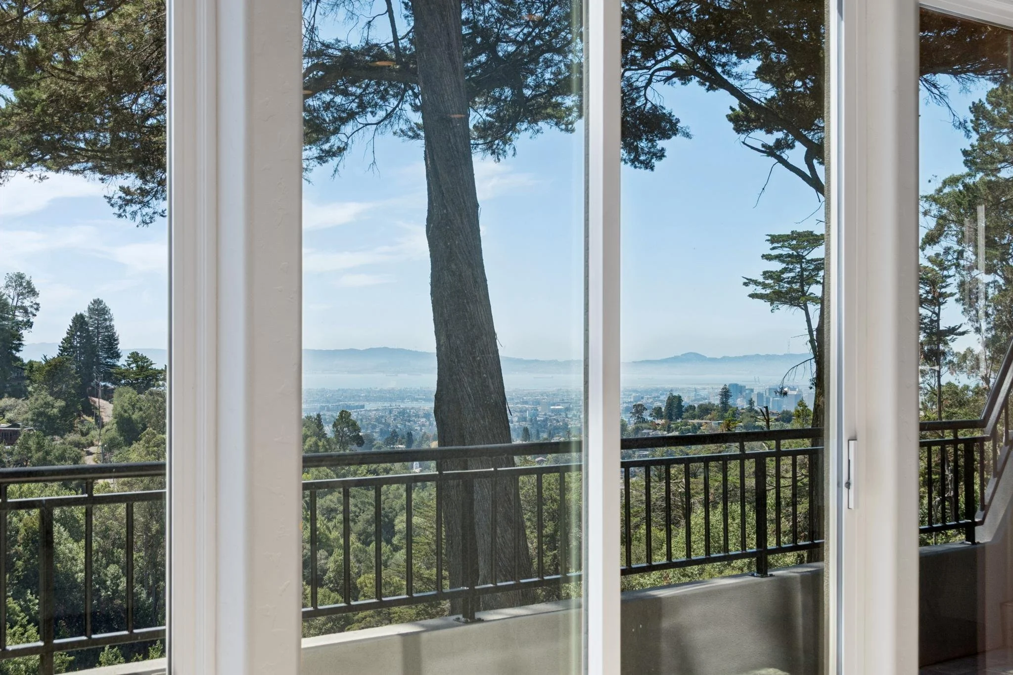 View through a large window showing trees, a hillside, and a body of water in the distance with a clear blue sky.