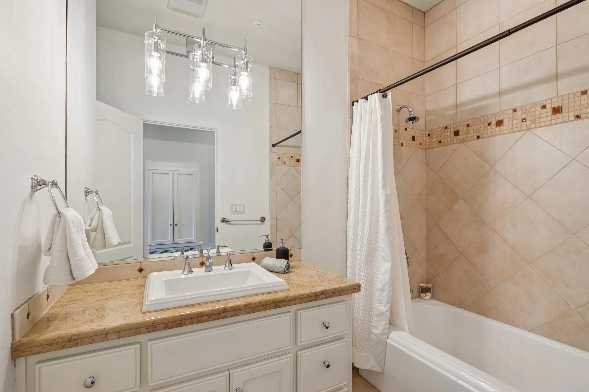 Bathroom with a mirror above a sink, beige tile shower with a shower curtain, white cabinets, and towels hanging on a silver towel bar.