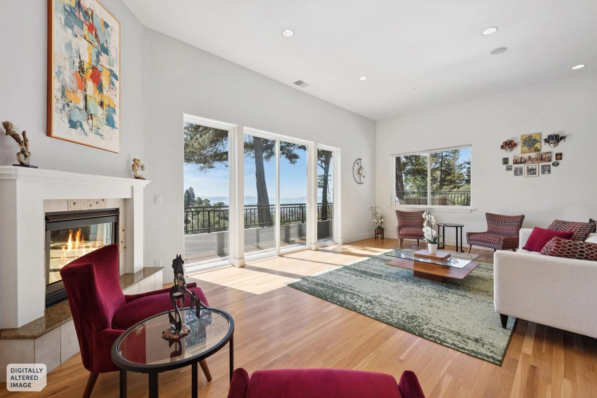 Bright living room with large windows showing trees outside, a fireplace with a fire, red velvet armchair, white sofa with red pillows, a glass-top coffee table, wall art, a clock, and a gallery wall with photos and masks.