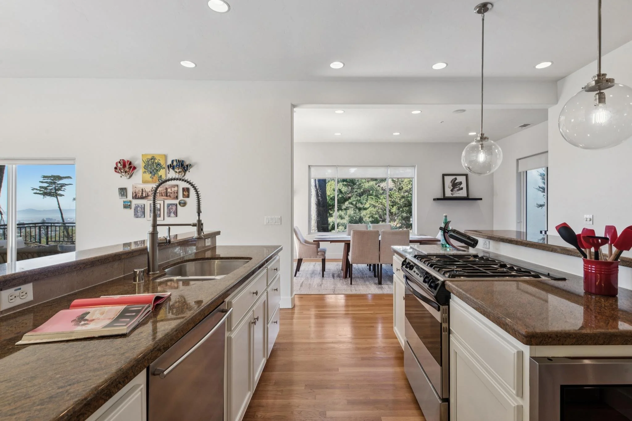 Modern kitchen with white cabinets, granite countertops, stainless steel appliances, and a view of a dining area with large windows showing trees outside.