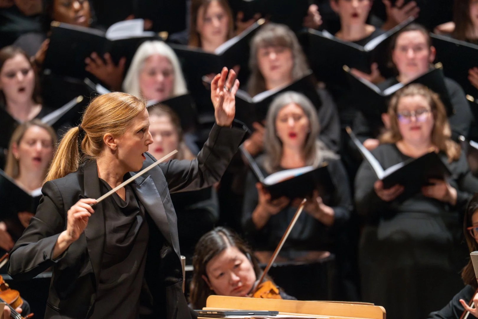 Conductor leading an orchestra with choir in the background.