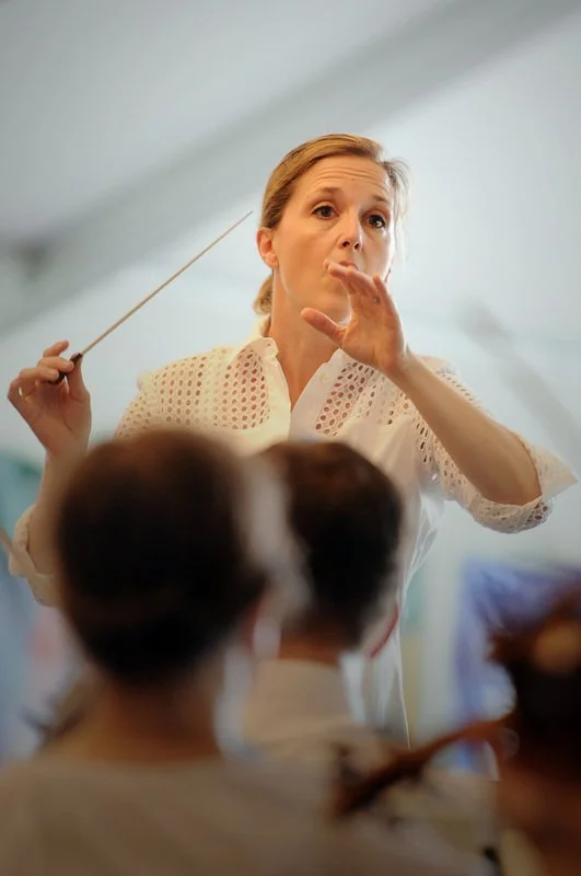 Erin Freeman conducting an orchestra, holding a baton in her right hand and gesturing with her left hand.