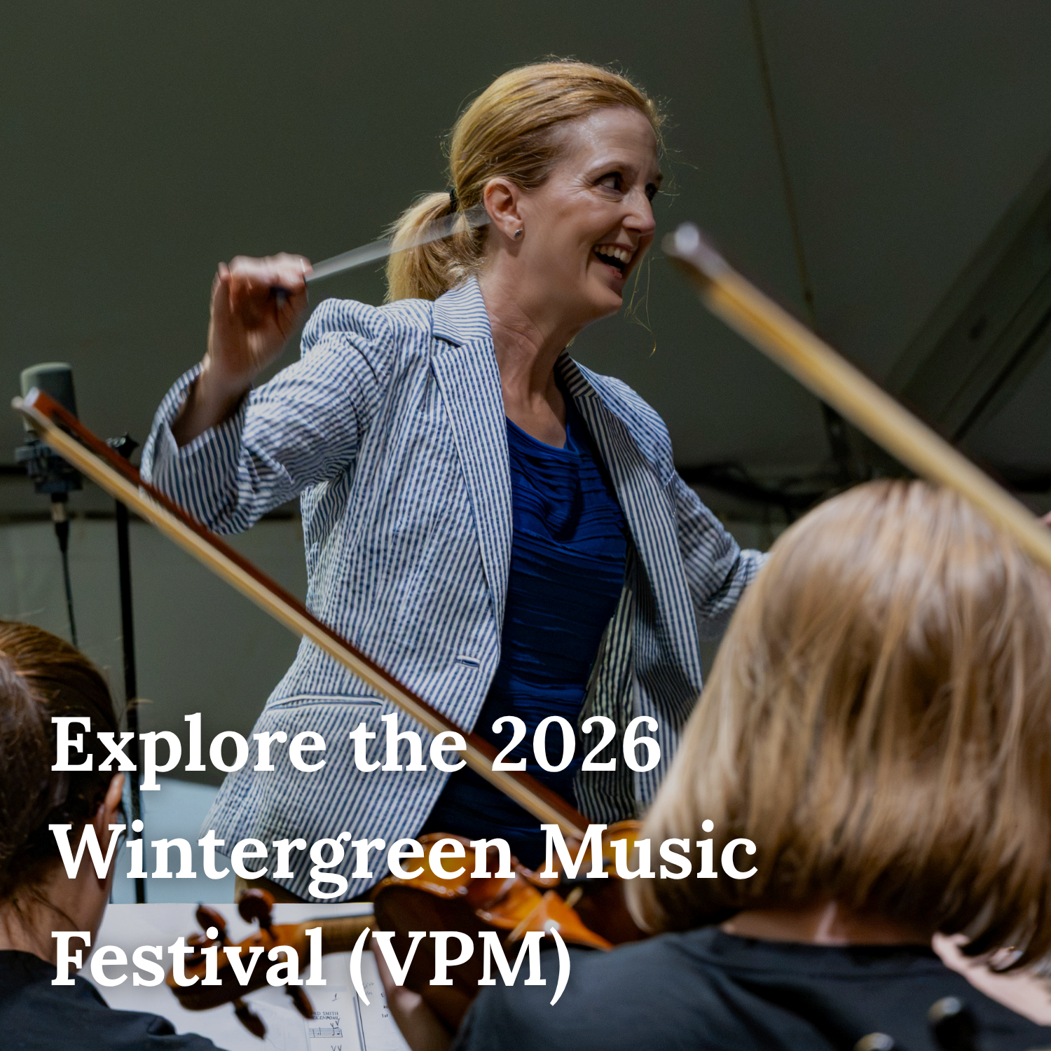 A woman conducting an orchestra during a music festival, with people playing violins in the foreground.
