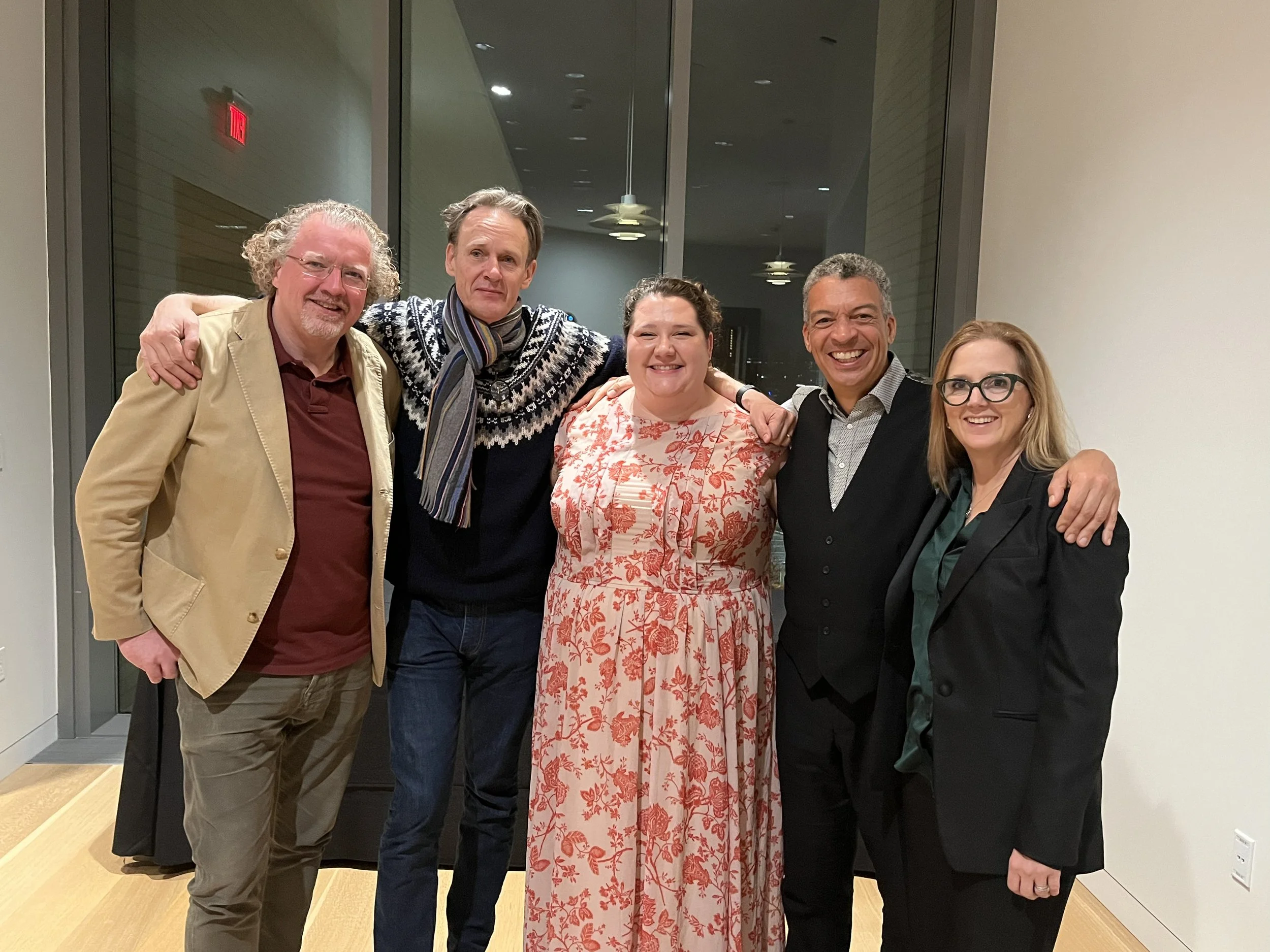 Stéphane Denève, Ian Bostridge, Felicia Moore, Roderick Williams, and Erin Freeman  standing together in an indoor setting, smiling for the camera with arms around each other, near large windows.