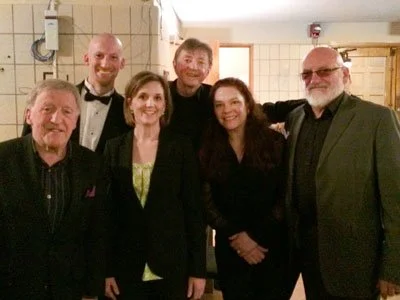 Group of six people dressed in formal attire posing indoors with smiling faces.