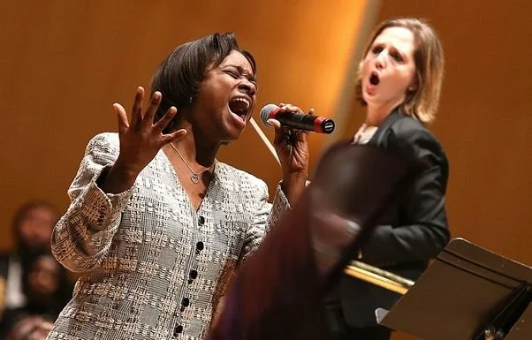 Erin Freeman conducting, with a soloist holding a microphone in the foreground and an orchestra in the background.