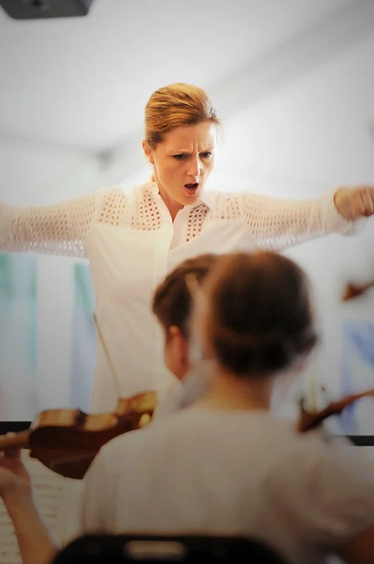 Erin Freeman conducting and orchestra with arms outstretched.