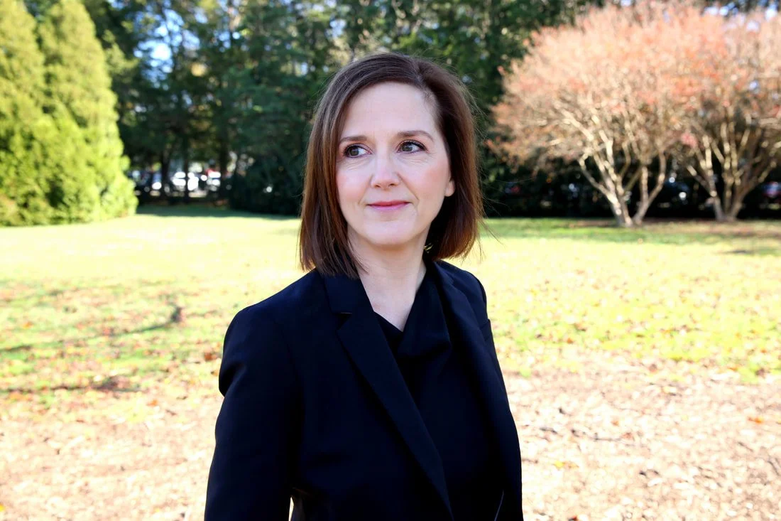 Erin Freeman wearing a black blazer outdoors in a park with trees and grass in the background.