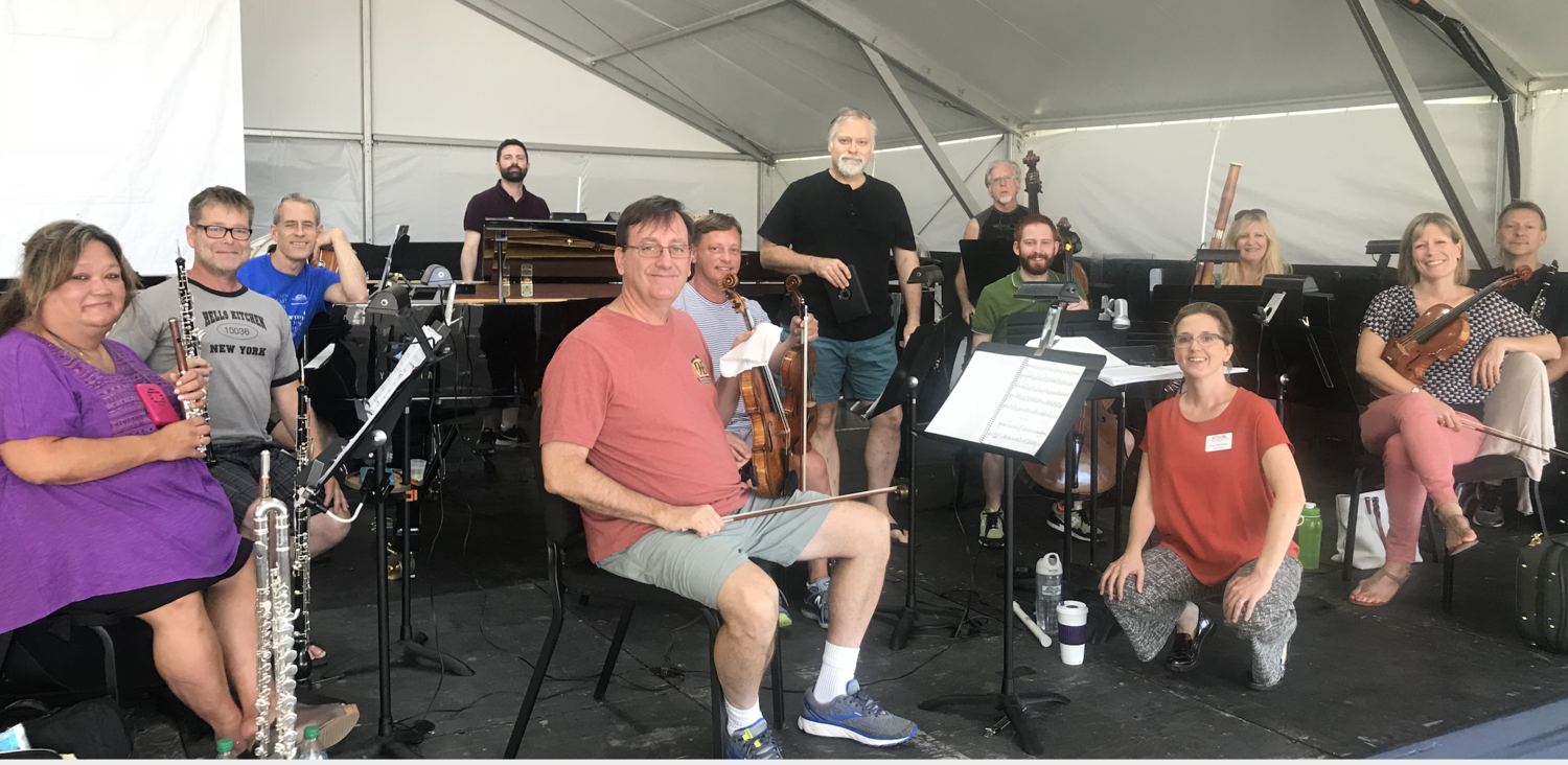 Group of musicians with various instruments in a large white tent during rehearsal or performance.