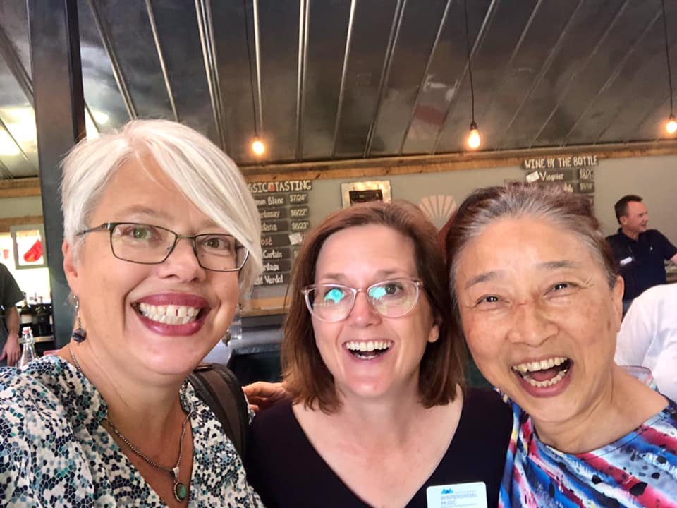 Three women smiling and taking a selfie in a restaurant or bar with a chalkboard menu in the background.