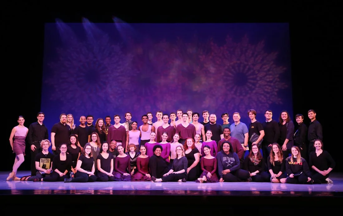 Group of theater performers posing on stage with purple and pink fireworks backdrop.