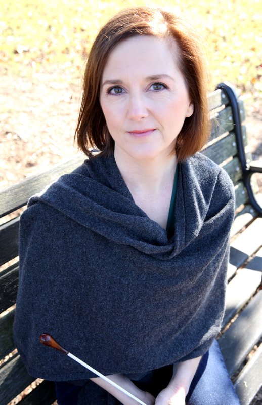 Erin Freeman sitting on a park bench outdoors with sunlight and fallen leaves in the background, wearing a dark gray shawl.