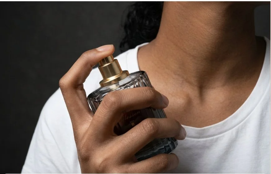 Person holding a glass perfume bottle with a gold spray nozzle.