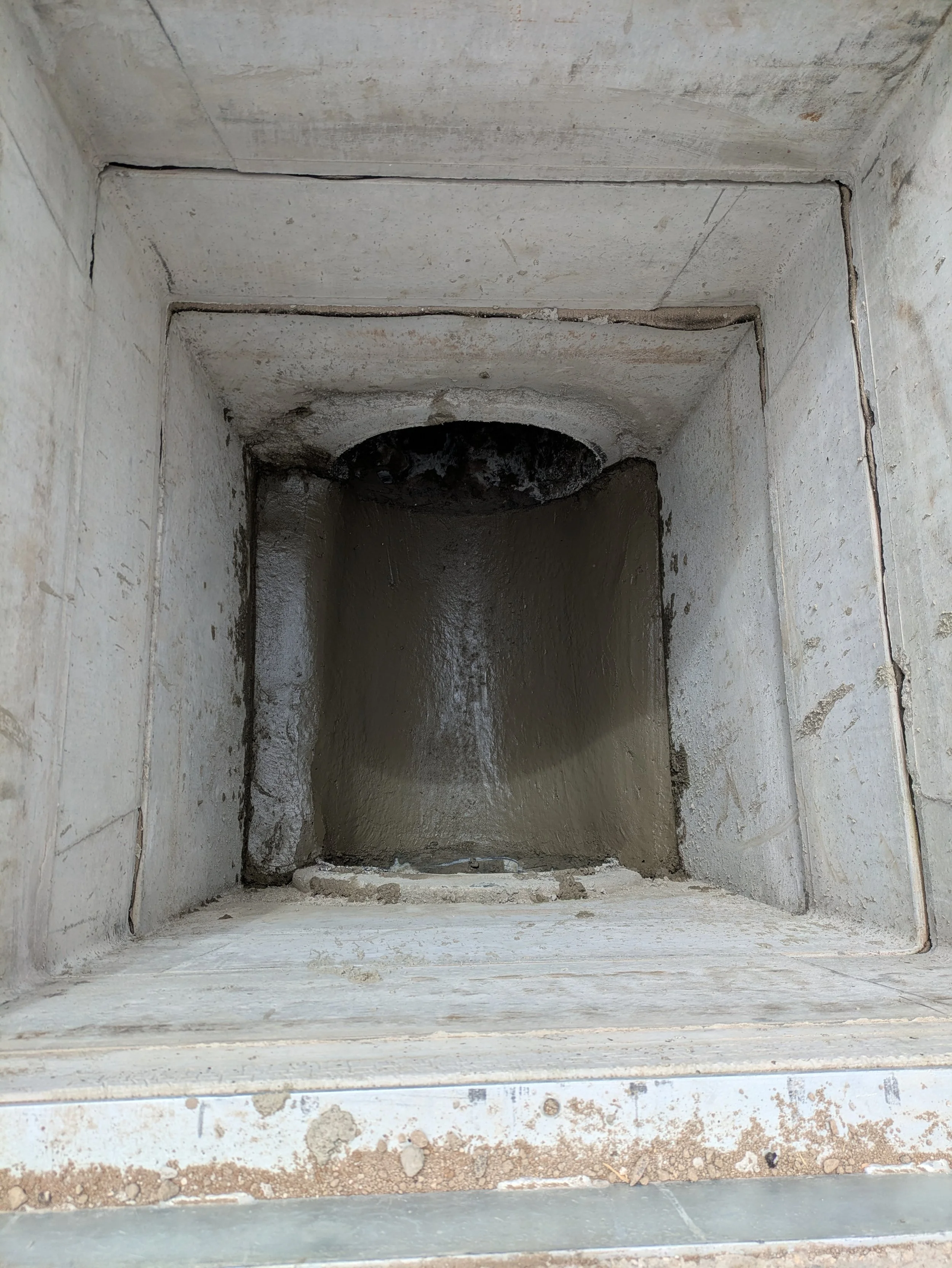 Close-up view of a square concrete sewer pipe with a rough interior, with some dirt and water inside.