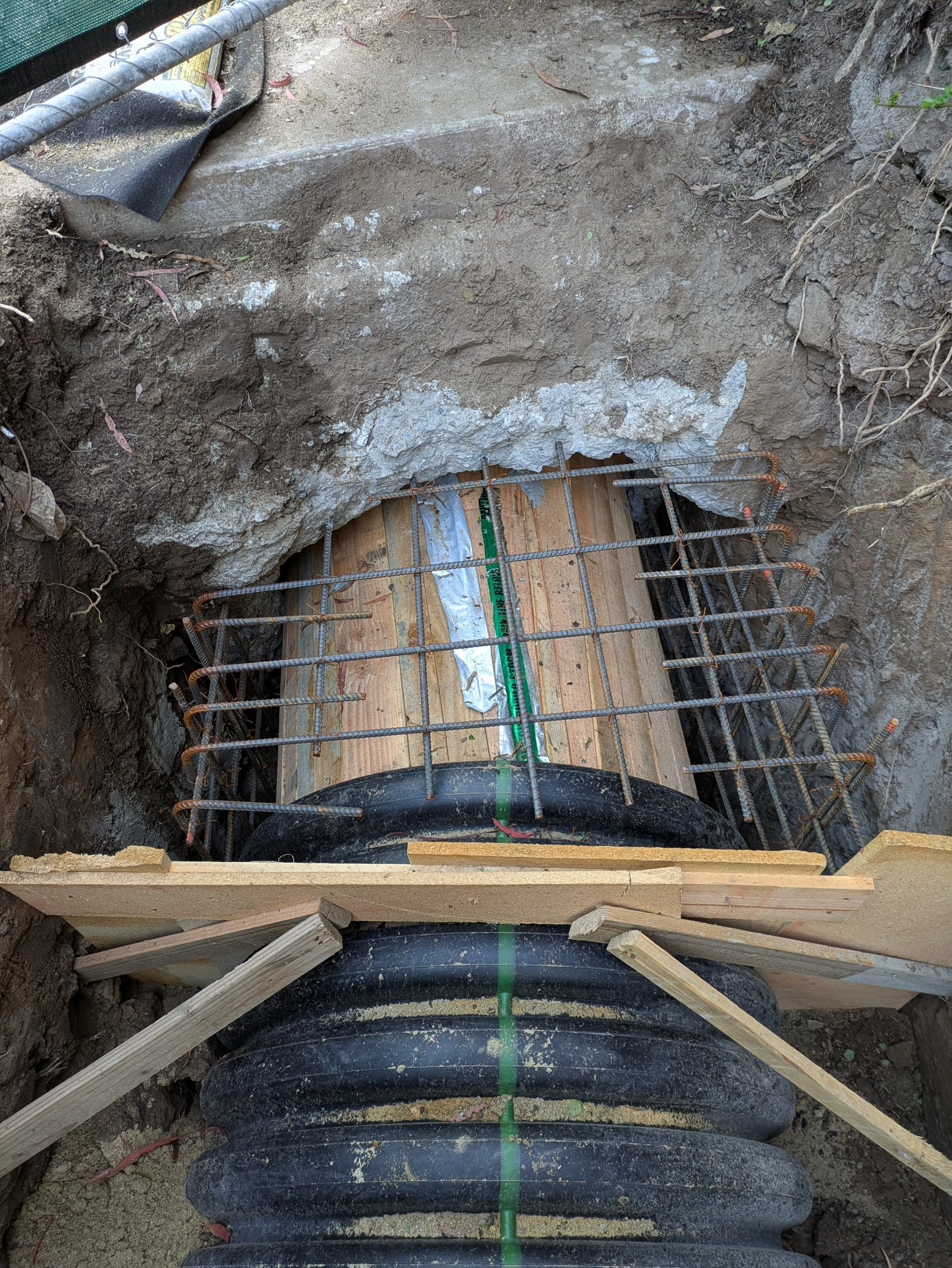 Underground utility trench with rebar reinforcements, wooden supporting forms, and surrounding dirt and soil.