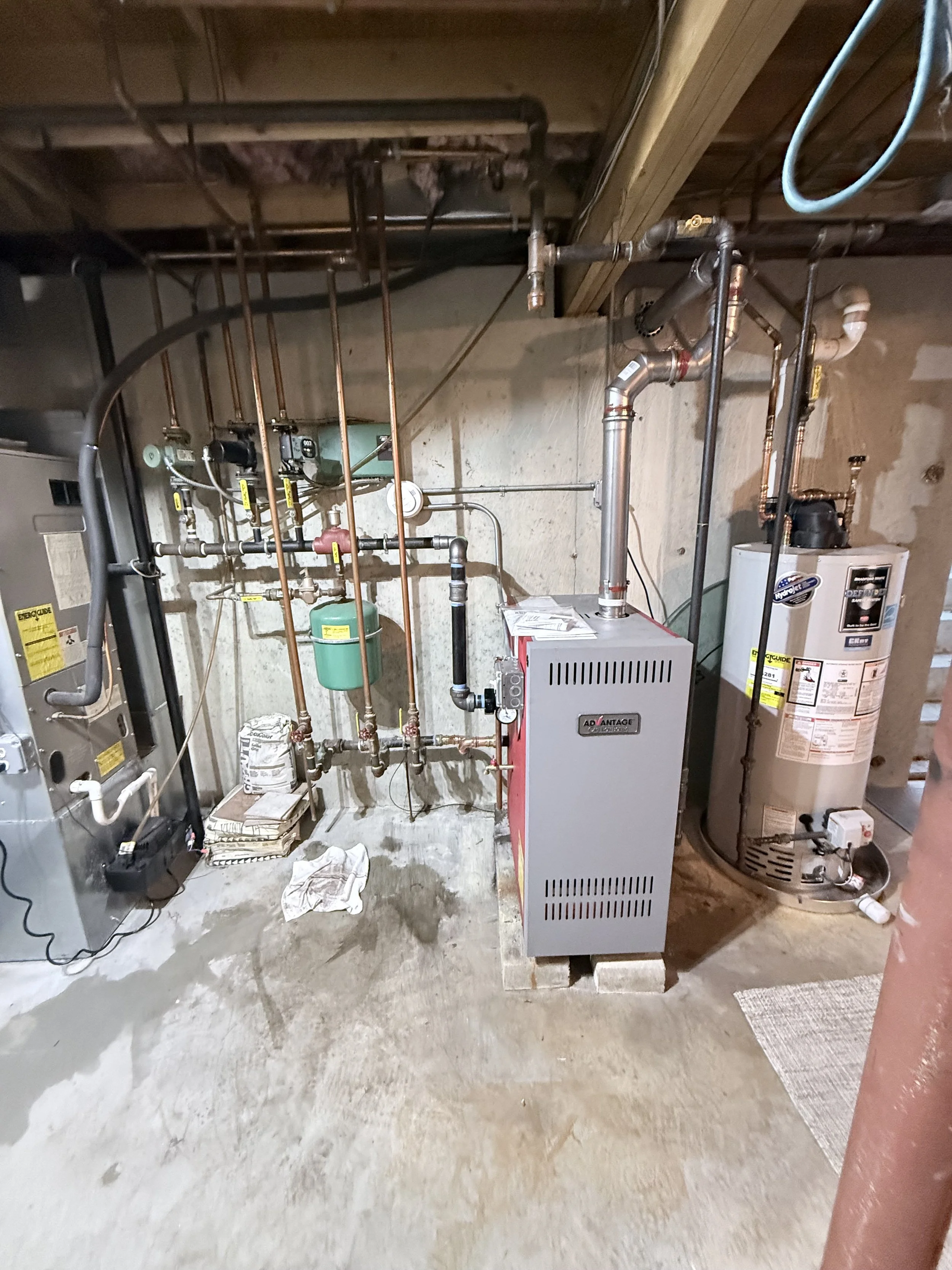 Basement utility area with a water heater, boiler, pipes, and miscellaneous items on the concrete floor.