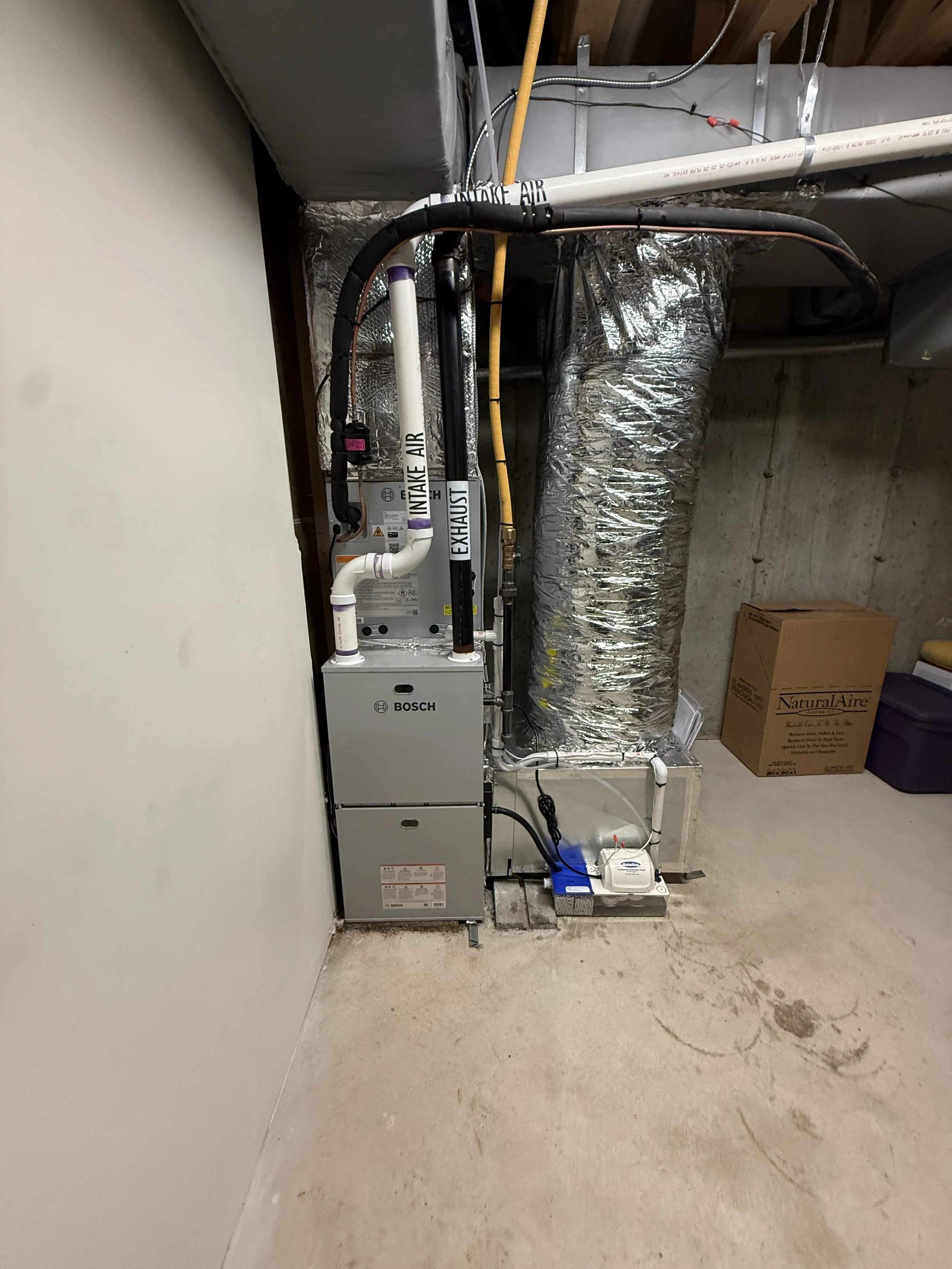 HVAC system with ducts, pipes, and a furnace installed in a basement, with cardboard boxes and storage containers nearby.