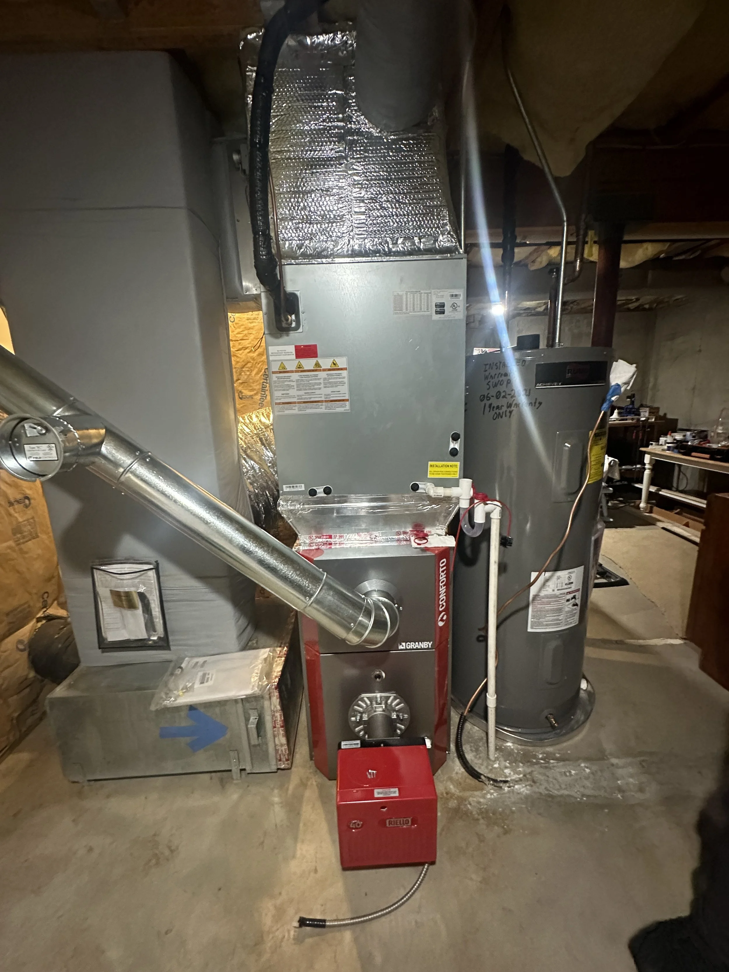 Photo of an HVAC system including a furnace, ductwork, and a red tool box in a basement with concrete floor and unfinished ceiling.
