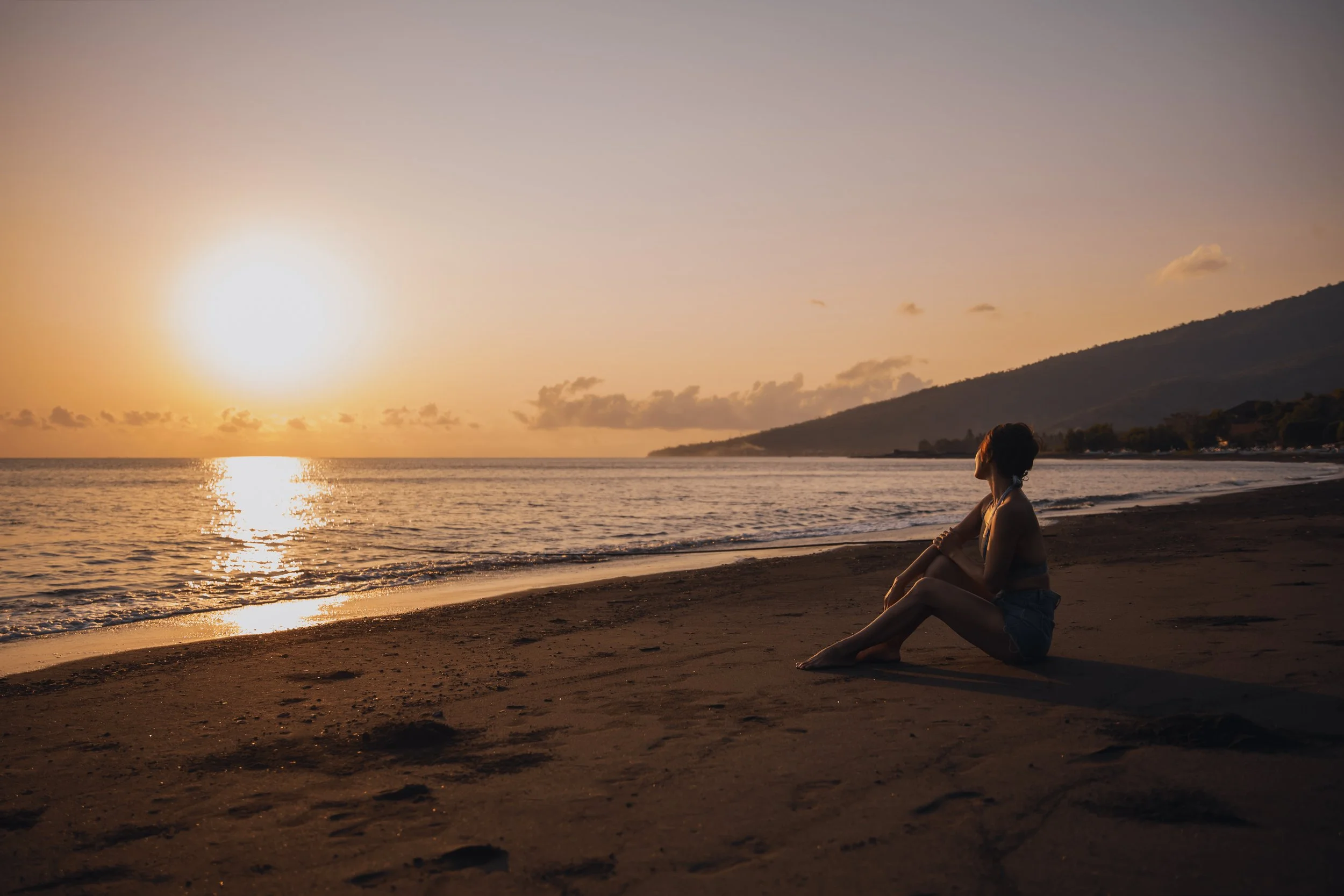 Person sitting on a beach at sunset, reflecting on their next life chapter