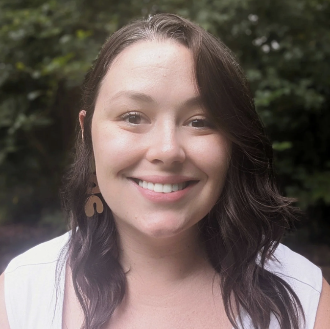 Kate Elkins smiling outdoors with greenery in the background.