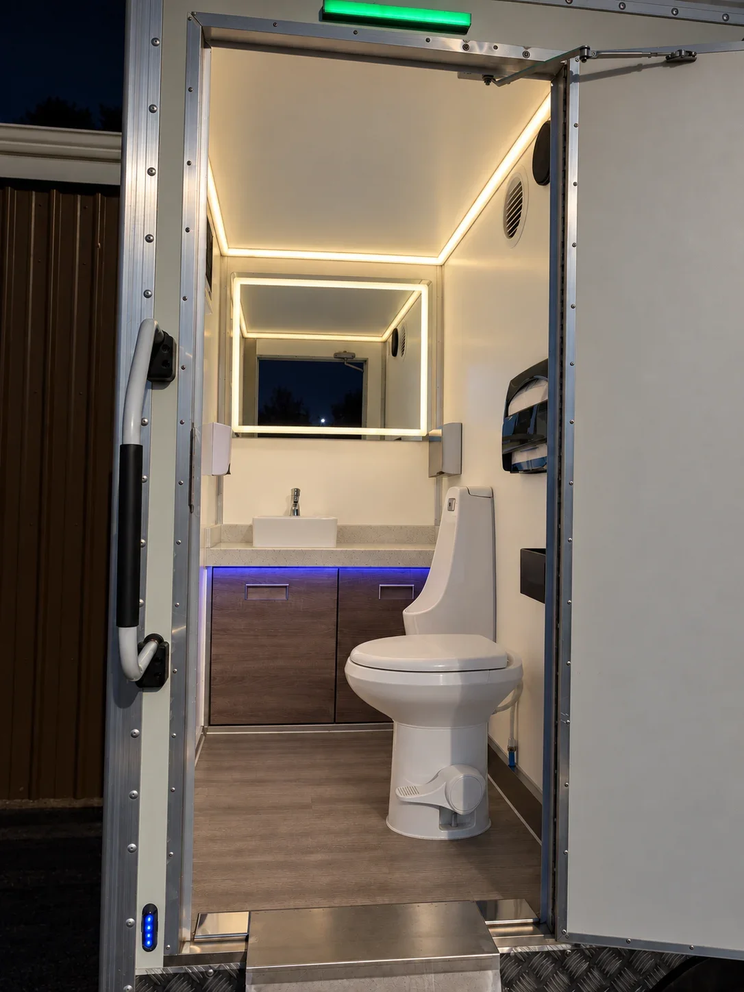 Restroom interior at night with warm-white ceiling and mirror lights and subtle under-counter accent lighting.