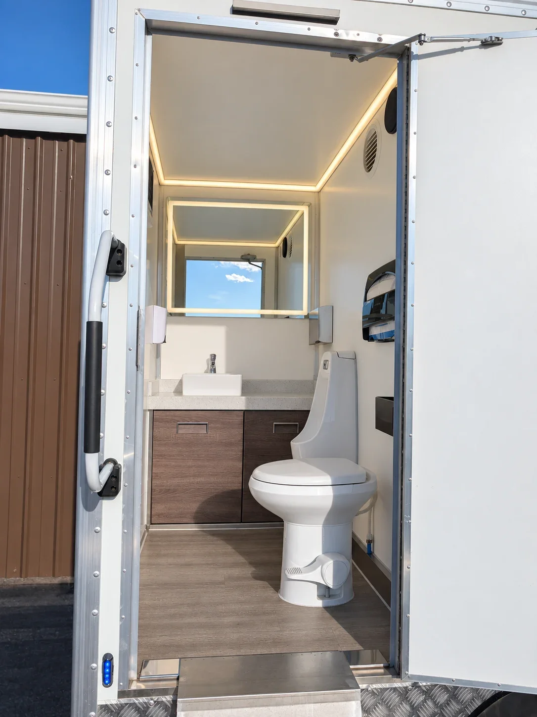 Compact restroom interior with a toilet, sink, woodgrain cabinet and illuminated ceiling and mirror.