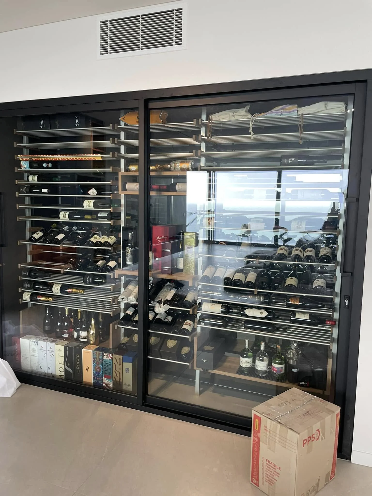 A wine cooler with glass doors filled with wine bottles, and a cardboard box on the floor nearby.