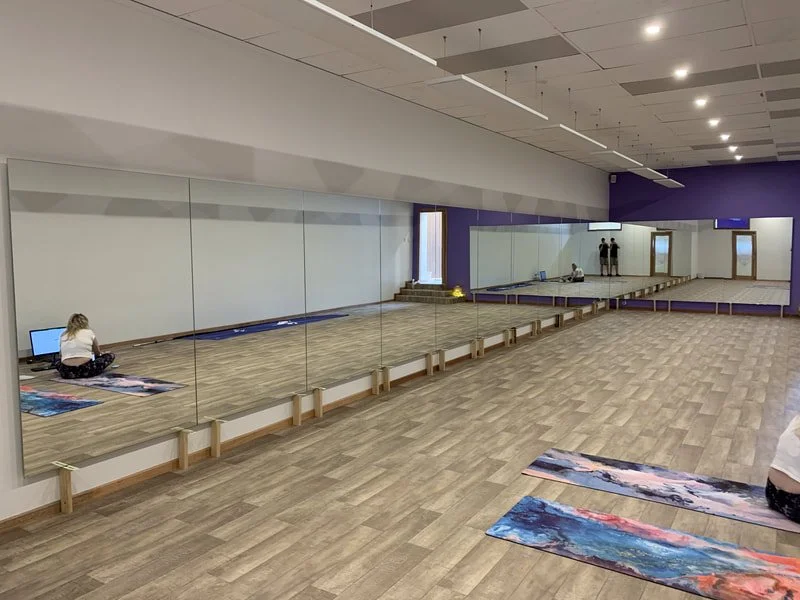 A yoga or meditation studio with large wall mirrors, wooden flooring, purple accent walls, and yoga mats laid out on the floor. 
